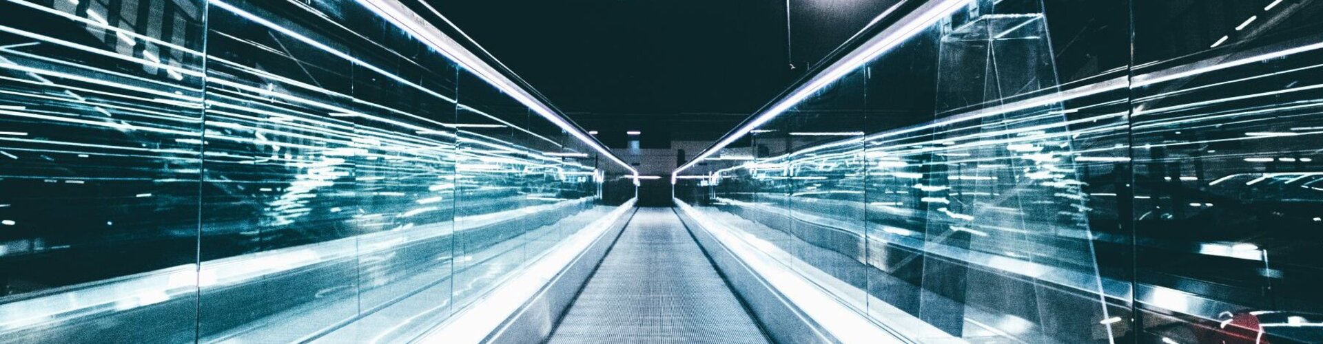 Blick von unten auf eine Fahrtreppe in Richtung eines dunklen Himmels mit futuristischen Lichtbewegungen