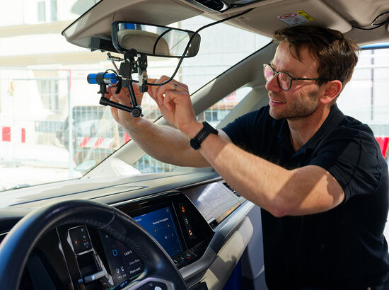 TÜV-Prüfer befestigt Teil der Messtechnik im Fahrzeug | © TÜV-Verband