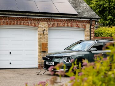 Bidirektionales Laden: Potenziale von E-Autos für das Stromnetz nutzen Ein Auto steht vor einem Garagentor und wird geladen. Es ist ein Elektorauto. Auf der Garage befindet sich eine Solaranlage.
