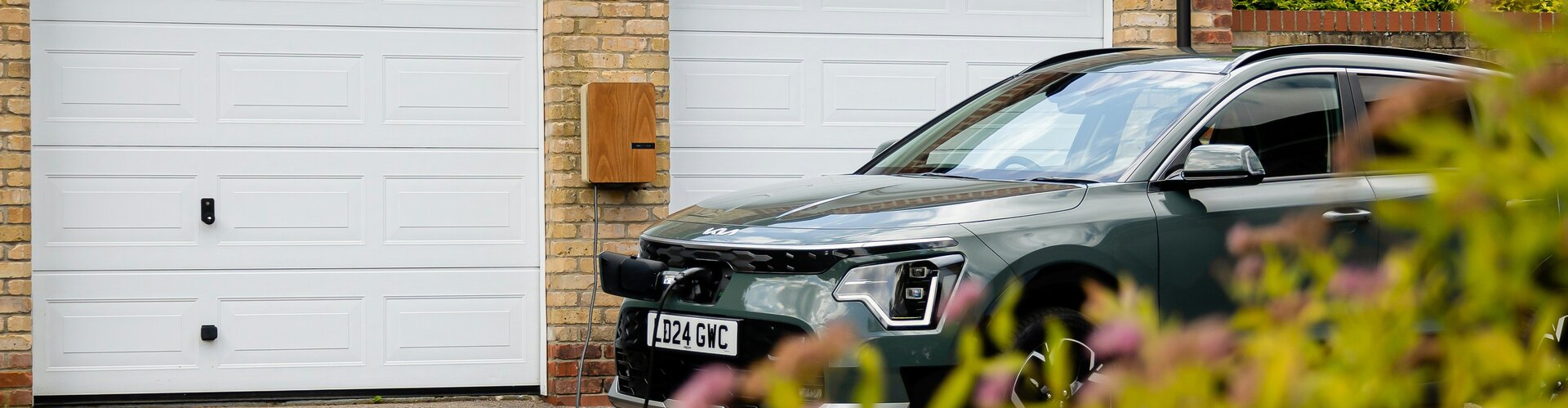 Bidirektionales Laden: Potenziale von E-Autos für das Stromnetz nutzen Ein Auto steht vor einem Garagentor und wird geladen. Es ist ein Elektorauto. Auf der Garage befindet sich eine Solaranlage.