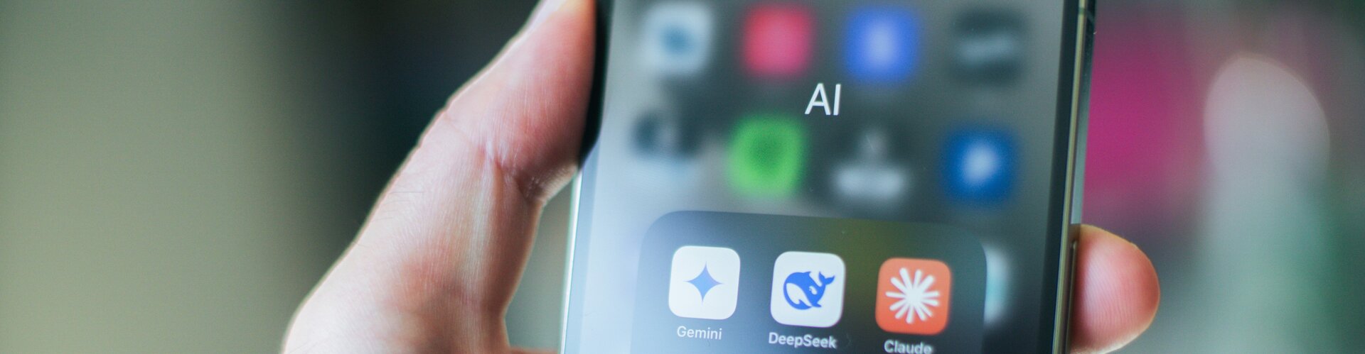 Neue KI-Kennzeichnungen: Inhalte besser erkennen und einordnen In der Hand hält jemand ein Handy. Auf dem Bildschirm ist ein Ordner geöffnet in dem sich verschiedene KI-Apps befinden. Beispielsweise Claude oder Chatgpt.