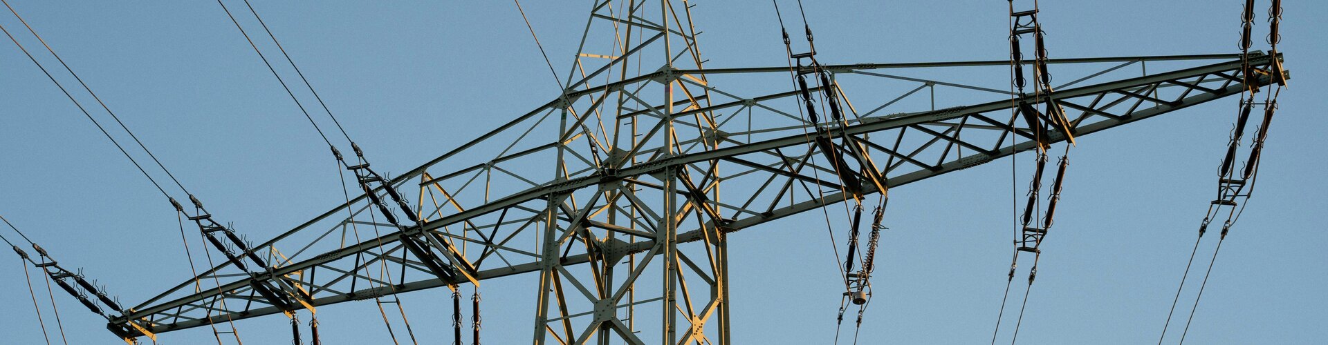 Hybride Angriffe: Infrastruktur ertüchtigen Ein hoher Strommast aus Stahlgitter gegen einen blauen Himmel.