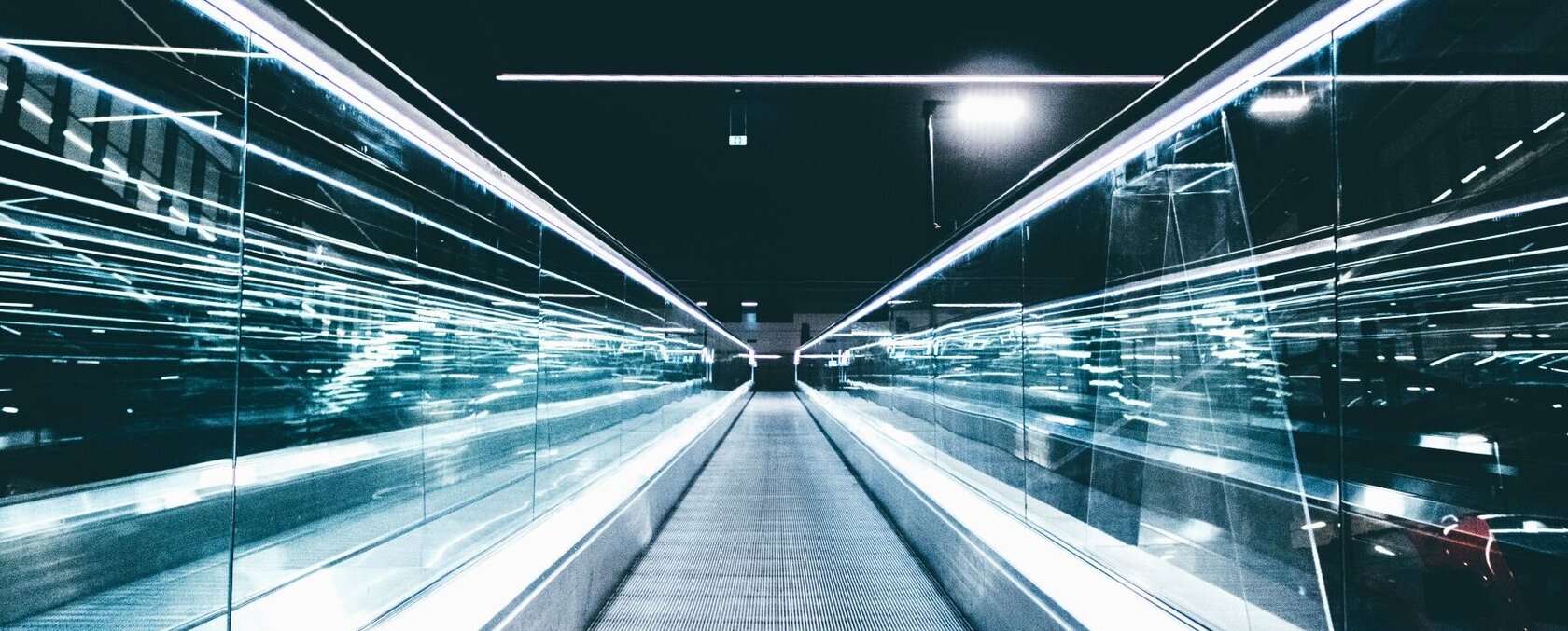 Blick von unten auf eine Fahrtreppe in Richtung eines dunklen Himmels mit futuristischen Lichtbewegungen