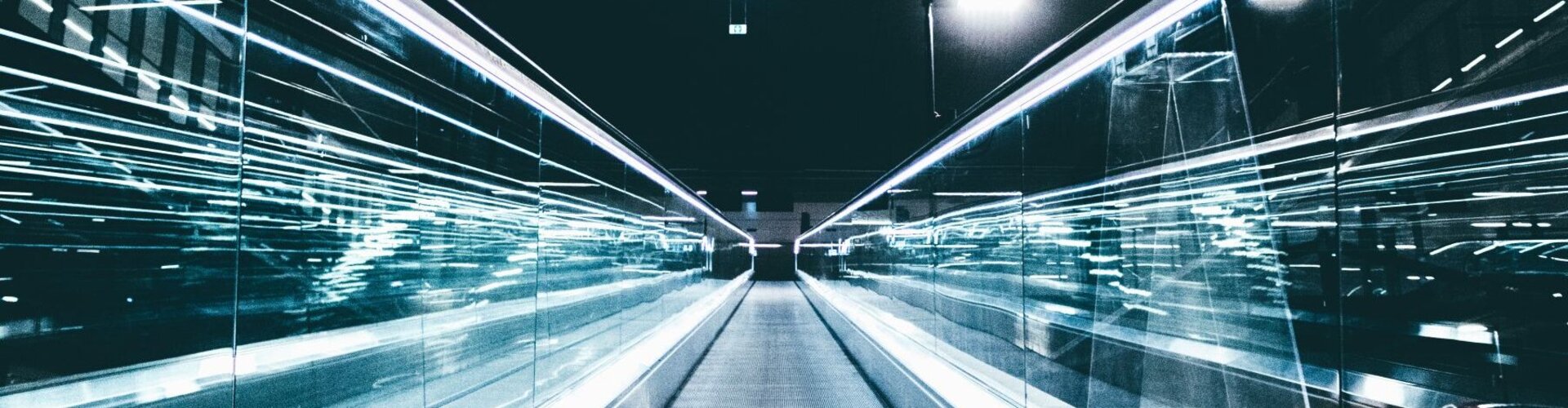 Blick von unten auf eine Fahrtreppe in Richtung eines dunklen Himmels mit futuristischen Lichtbewegungen