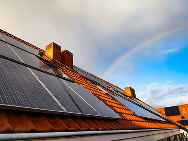 Dach eines Einfamilienhauses mit Solarpaneelen, über das sich ein Regenbogen neigt