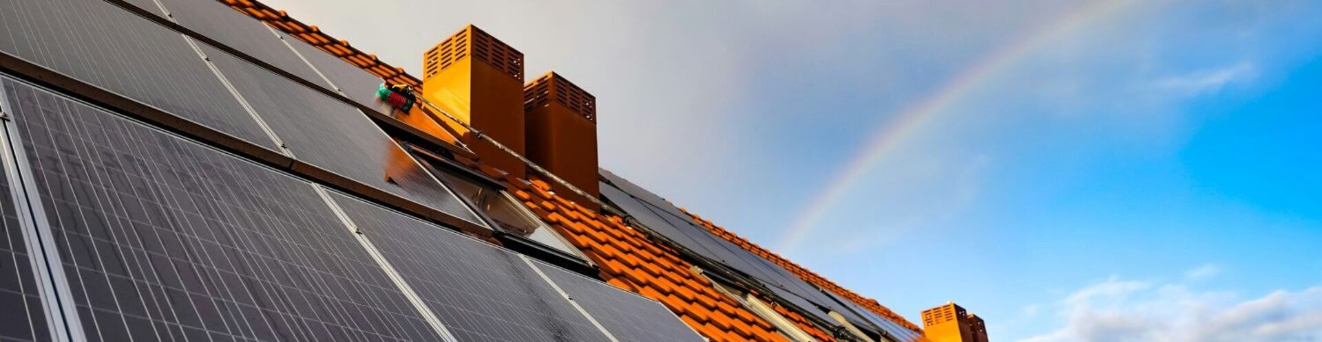 Dach eines Einfamilienhauses mit Solarpaneelen, über das sich ein Regenbogen neigt