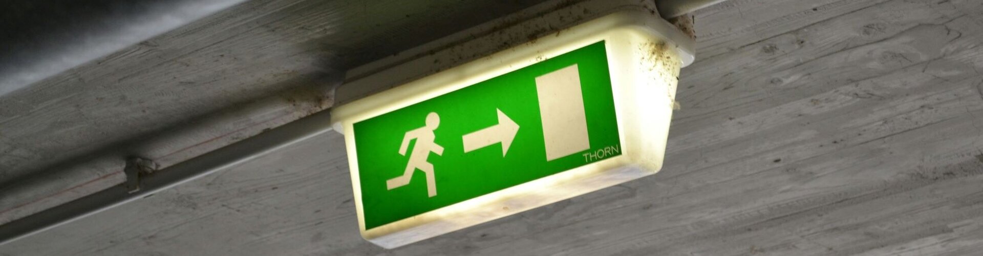 Ein beleuchtet Notausgangsschild hängt an einer Betondecke