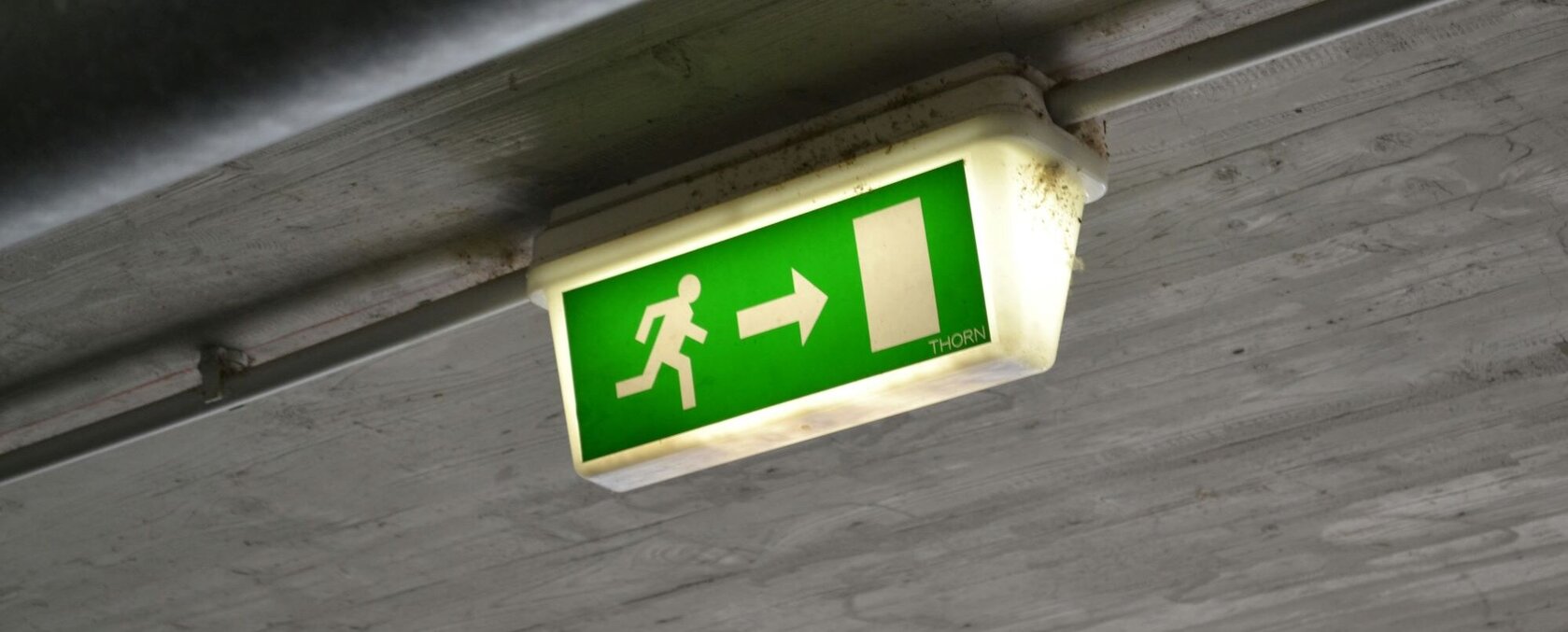 Ein beleuchtet Notausgangsschild hängt an einer Betondecke