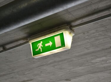 Ein beleuchtet Notausgangsschild hängt an einer Betondecke