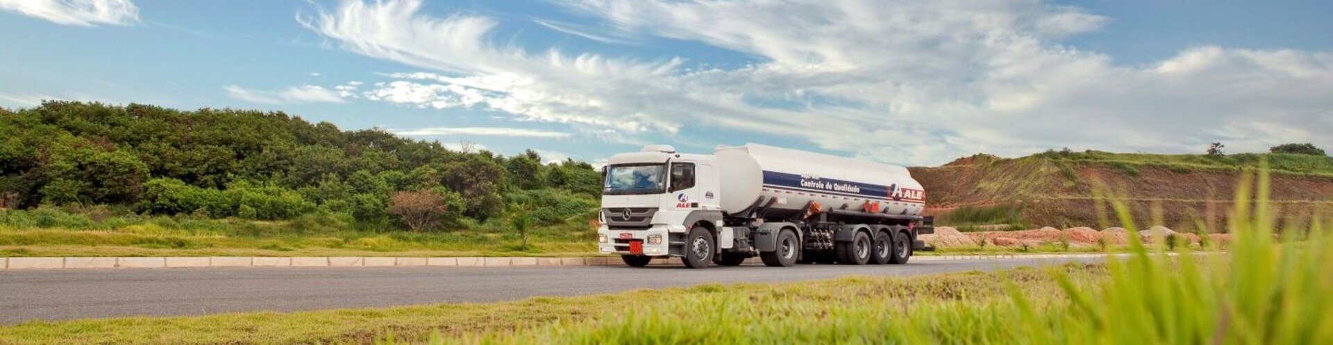 Ein Tanklastwagen fährt über eine Landstraße durch grüne Felder unter blauem Himmel