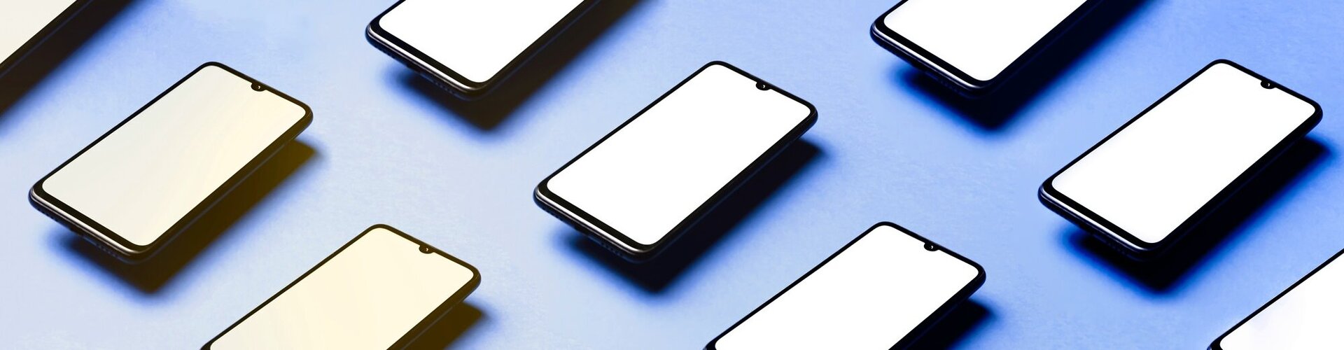 Diverse Smartphones liegen parallel nebeneinander angeordnet auf einem blauen Untergrund