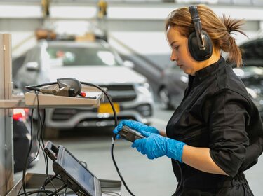 Eine Mechanikerin steht in einer Autowerkstatt an einem Laptop