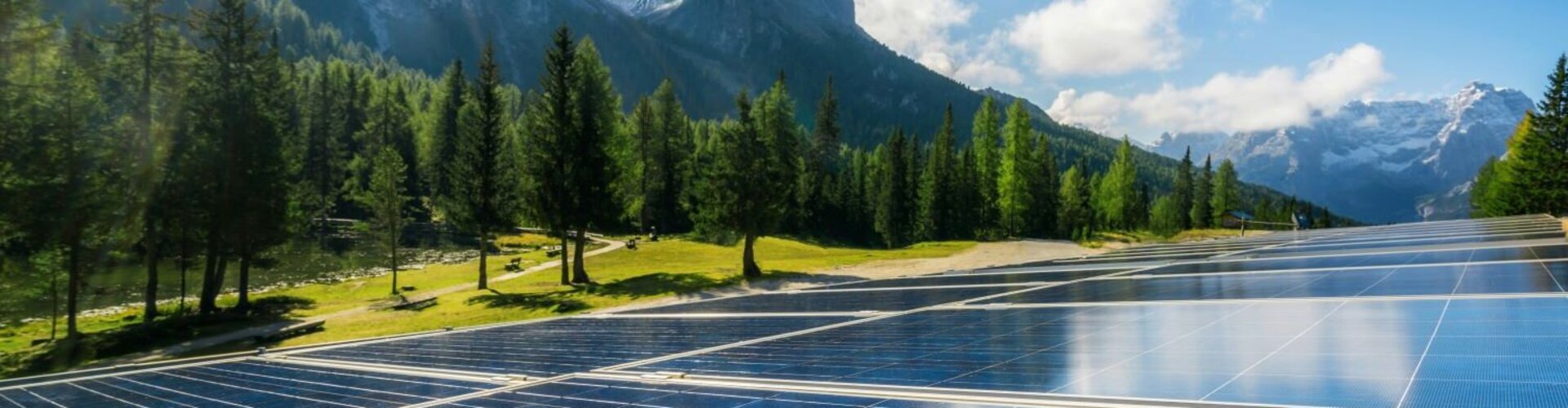 Solarpaneele, die auf einer grünen Wiese vor einem Bergpanorama stehen
