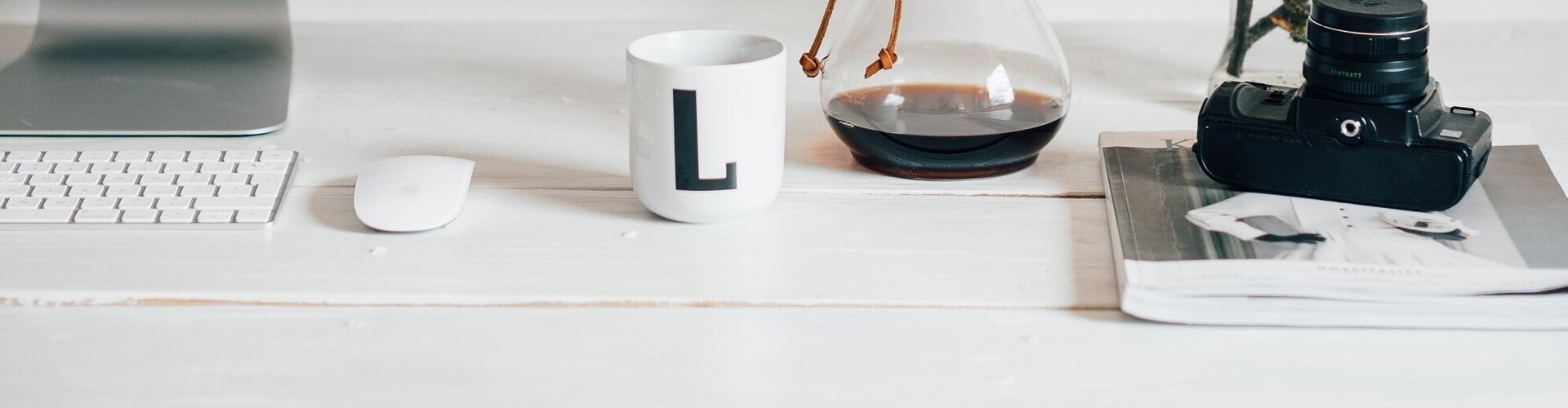 weißer Schreibtisch mit großem Bildschirm daneben steht eine Kaffeekanne und ein Strauch blühender Apfelzweige
