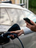 Eine Frau wartet vor einem Elektroauto darauf, dass ihr Fahrzeug fertig geladen ist