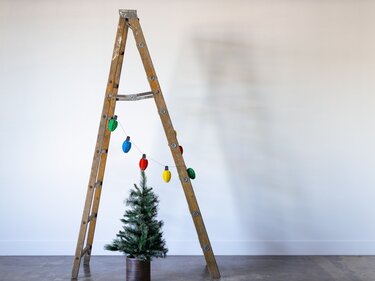Arbeiten über Kopf: Sicherheitstipps für Kauf und Verwendung von Leitern In einem Zimmer steht eine Leiter, an der eine Lichterkette hängt, und unter ihr steht ein kleiner geschmückter Weihnachtsbaum