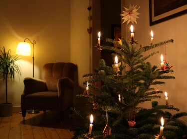 TÜV-Verband: Brände in der Weihnachtszeit verhindern Brennende Kerzen an Weihnachtsbaum im Wohnzimmer