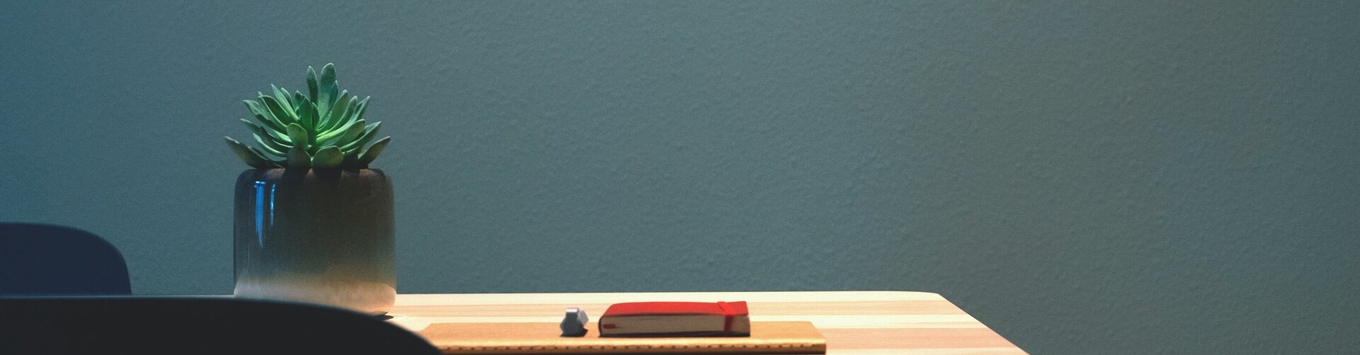 Dunkler Sessel vor hellem Tisch mit Vase und Buch 