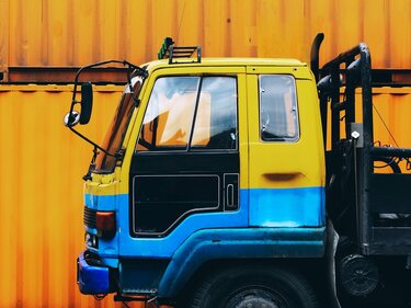 Seitenansicht der Fahrerkabine eines Lastwagens, der vor einem großen gelben Container steht