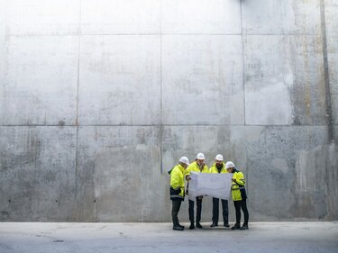 Abschaffung von Sicherheitsbeauftragten gefährdet den Arbeitsschutz Auf einer Baustelle stehen vier Personen in reflektierender Sicherheitskleidung mit Schutzhelmen