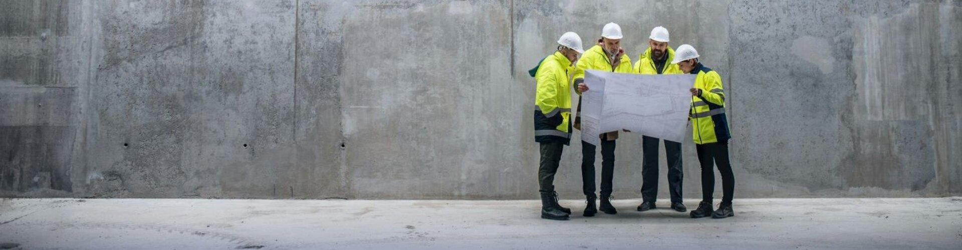 Auf einer Baustelle stehen vier Personen in reflektierender Sicherheitskleidung mit Schutzhelmen