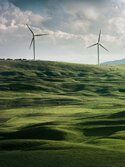 Grüne, hügelige Landschaft mit Windrädern im Hintergrund