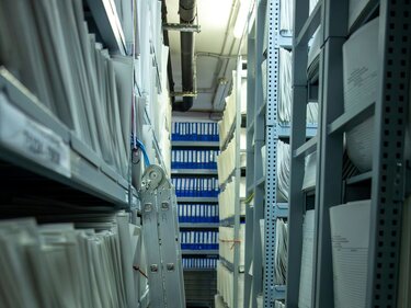 Geplante EU-Änderungen zu MDR/IVDR: TÜV-Verband und IG-NB plädieren für praxistaugliche Umsetzung bei Benannten Stellen Blick in einen Kellerraum, in dem sich die Last der Bürokratie in Form voller Bücherregale und überquellender Ordner zeigt