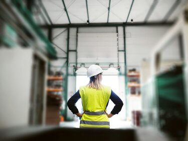 Eine Frau mit Sicherheitsweste und Schutzhelm steht in einer Lagerhalle