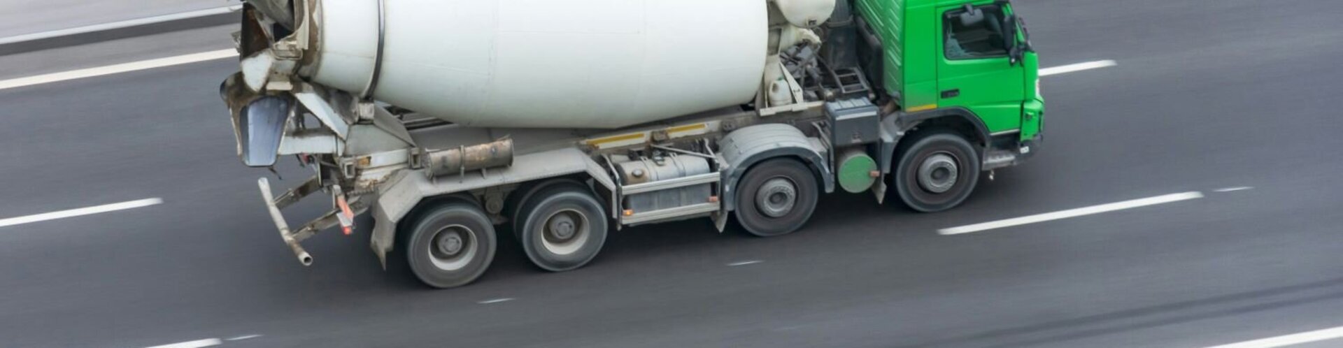 Ein Betonmischer mit grünem Fahrerhaus fährt auf einer Autobahn