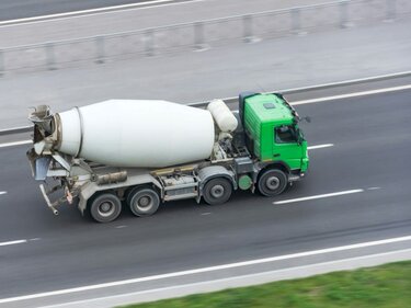 Ein Betonmischer mit grünem Fahrerhaus fährt auf einer Autobahn