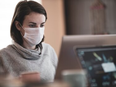 Braunhaarige Frau mit FFP-Maske arbeitet an Computer