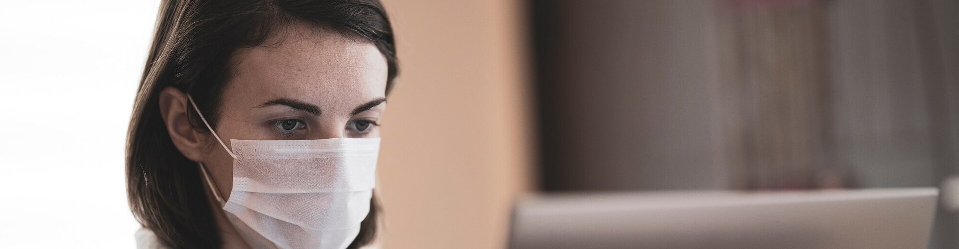 Braunhaarige Frau mit FFP-Maske arbeitet an Computer