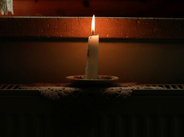 Eine Kerze steht auf einer Heizung und beleuchtet einen ansonsten dunklenRaum