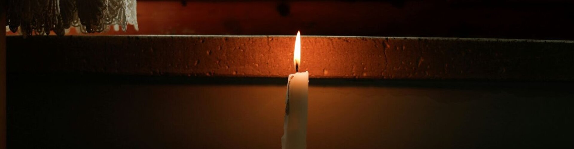 Eine Kerze steht auf einer Heizung und beleuchtet einen ansonsten dunklenRaum