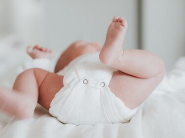 TÜV-Verband: Nicht jeder Heizstrahler für Einsatz am Wickeltisch geeignet Baby in weißer Windel liegt auf weißer Decke und strampelt mit nackten Beinen