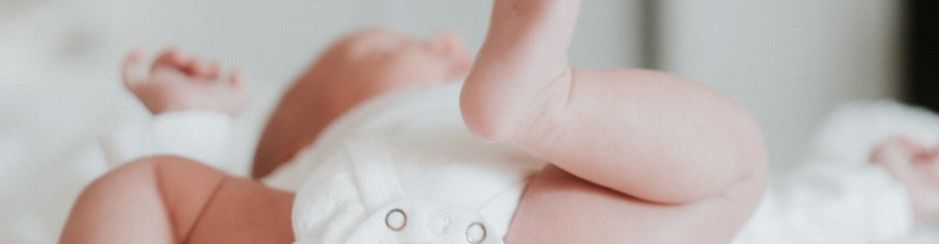 Baby in weißer Windel liegt auf weißer Decke und strampelt mit nackten Beinen