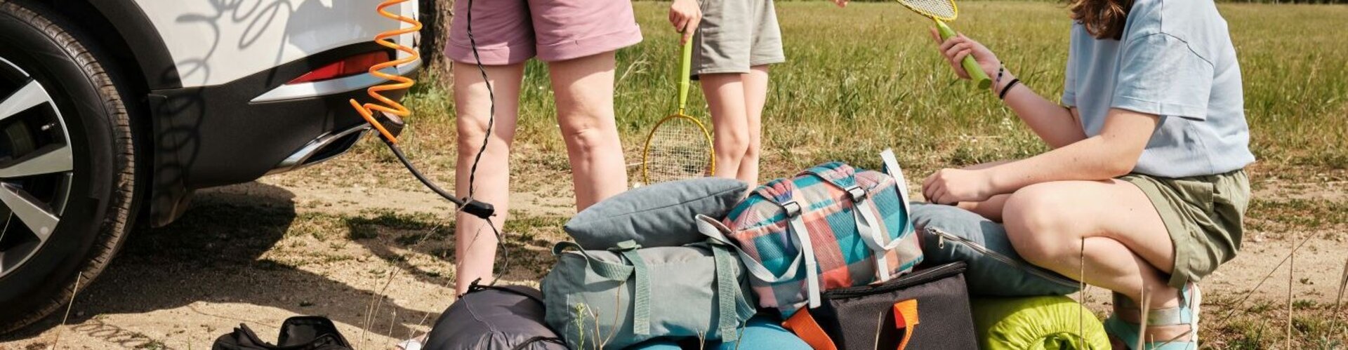 Eine Mutter und ihre Töchter stehen am Kofferraum eines weißen Autos vor einer Menge Gepäck