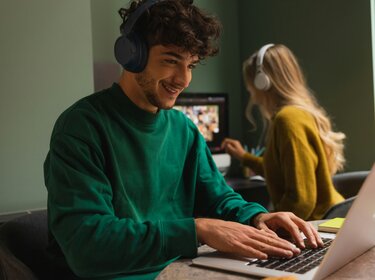 Junger Mann arbeitet am Laptop und hört Musik über Kopfhörer.
