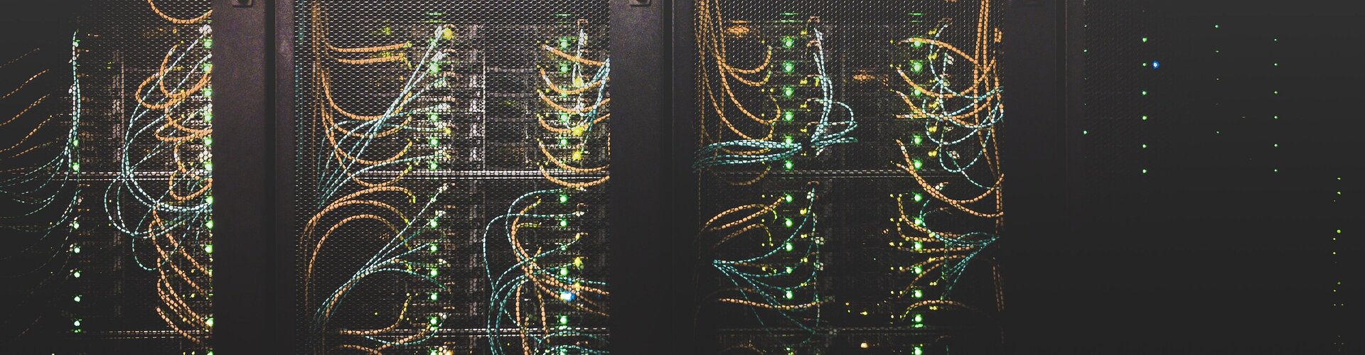 Blick auf Serverracks in einem Rechenzentrum mit zahlreichen vernetzten Kabeln und leuchtenden Statusanzeigen – Symbol für IT-Infrastruktur und Cybersicherheit