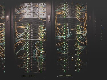 Blick auf Serverracks in einem Rechenzentrum mit zahlreichen vernetzten Kabeln und leuchtenden Statusanzeigen – Symbol für IT-Infrastruktur und Cybersicherheit