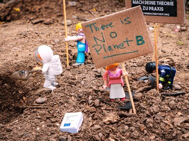 Spielfiguren, die auf Erde stehen und Demonstrationsplakate für eine Klimademo in der Hand halten