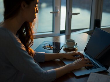 Frau mit langen Locken arbeitet am Laptop, neben ihr steht eine Tasse Kaffee