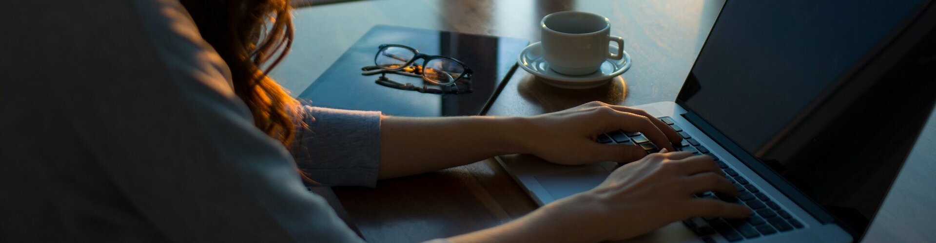 Frau mit langen Locken arbeitet am Laptop, neben ihr steht eine Tasse Kaffee