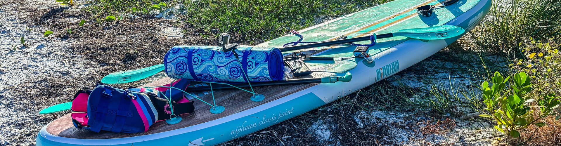 SUP-Sommer: Board vor der ersten Tour gründlich prüfen blau-weißes Stand-Up-Paddle-Board liegt am Strand im Sonnenschein