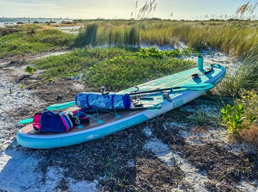 blau-weißes Stand-Up-Paddle-Board liegt am Strand im Sonnenschein