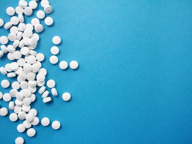 Start der Erkältungssaison: Achtung beim Autofahren unter Medikamenteneinfluss Ein Haufen weißer Tabletten liegt auf einem blauen Untergrund