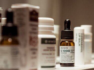 Blick auf ein Regalbrett mit diversen Medizinbehältern - im Fokus ein Pipettenfläschchen mit Medizinalcannabis