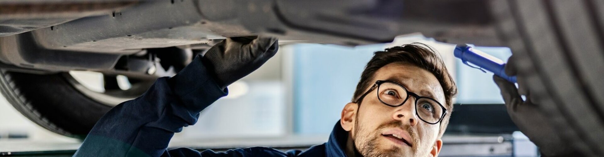 Ein Mann steht in der Montagegrube unter einem Pkw und leichtet die Unterseite des Fahrzeugs mit einer Taschenlampe an