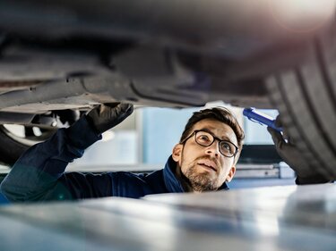 Ein Mann steht in der Montagegrube unter einem Pkw und leichtet die Unterseite des Fahrzeugs mit einer Taschenlampe an