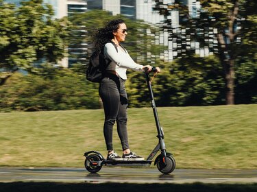 Steigende E-Scooter-Unfallzahlen: Sicherheit muss mit der Mobilitätswende Schritt halten Frau fährt auf einem E-Scooter durch einen Park